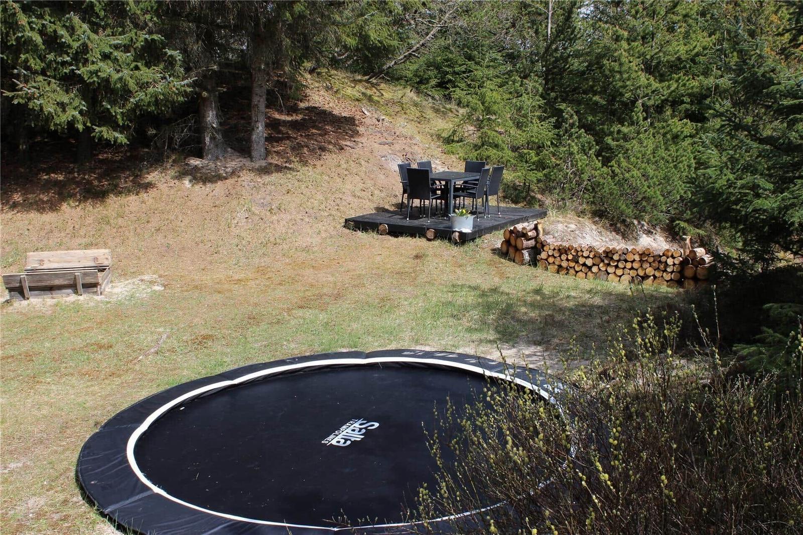 Außenbereich mit Trampolin, Holzstapel und Sitzplatz auf Terrasse.