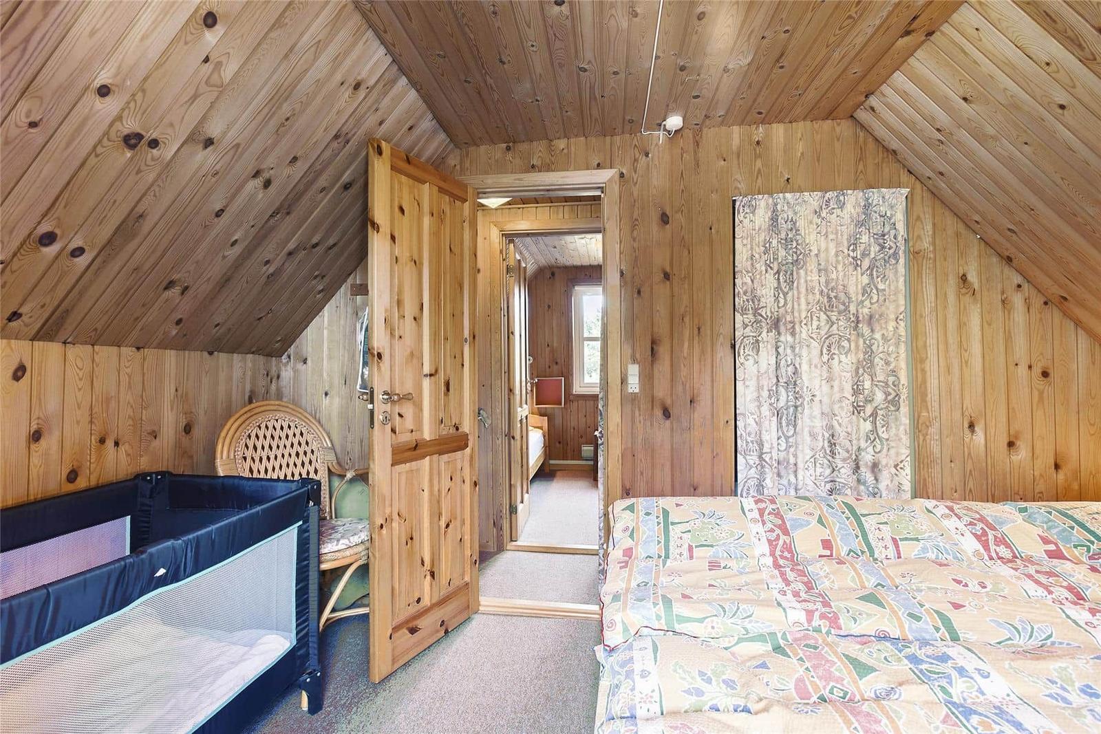 Schlafzimmer mit Holzwand, Bett, Kinderbett und Tür zu einem weiteren Raum.