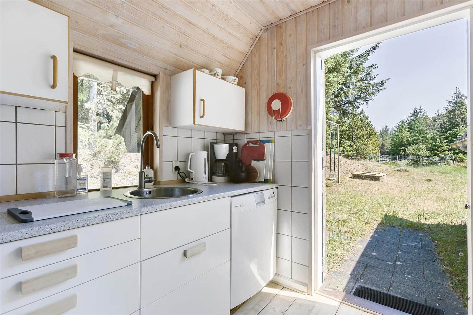 Küche mit Spüle, Kaffeemaschine und Waschmaschine. Durchgang zu einem Garten mit Bäumen.