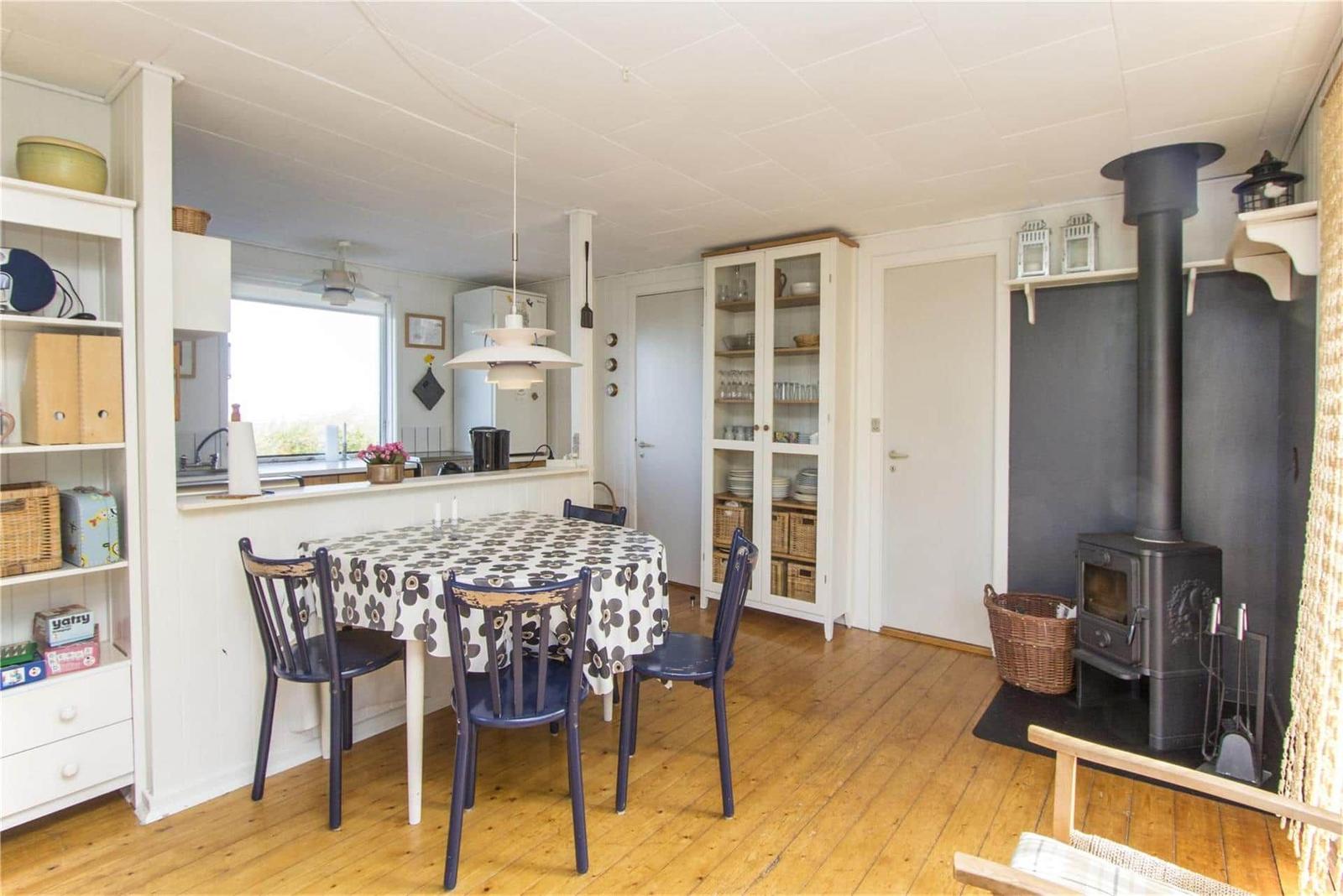 Dining area with table, chairs, and wooden floor. Fireplace and kitchen visible.