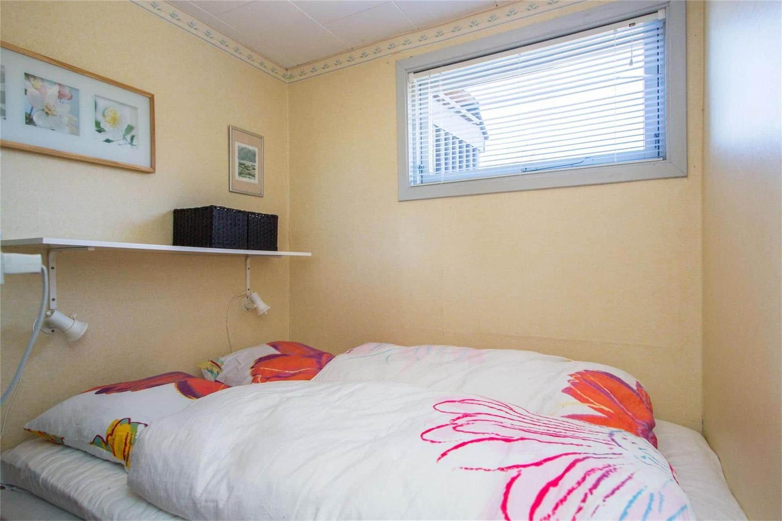 Bedroom with bed, window, and wall shelf with pictures.