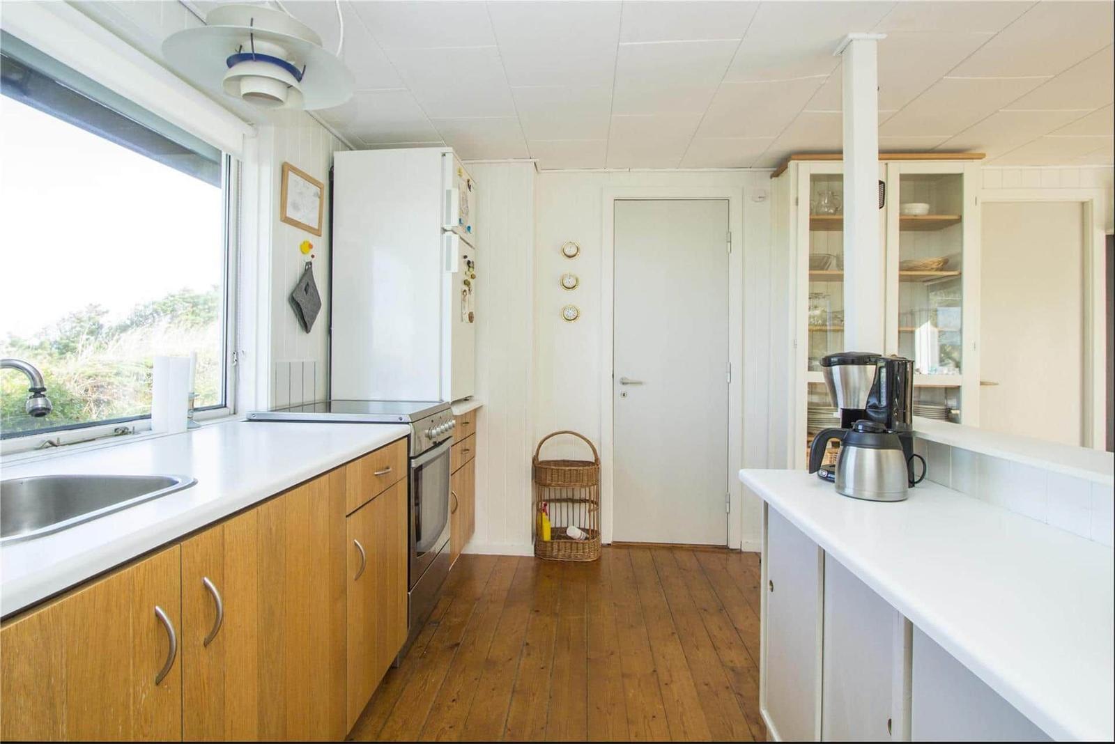 Kitchen with wooden floor, white cabinets, and window. Refrigerator, stove, and sink visible.