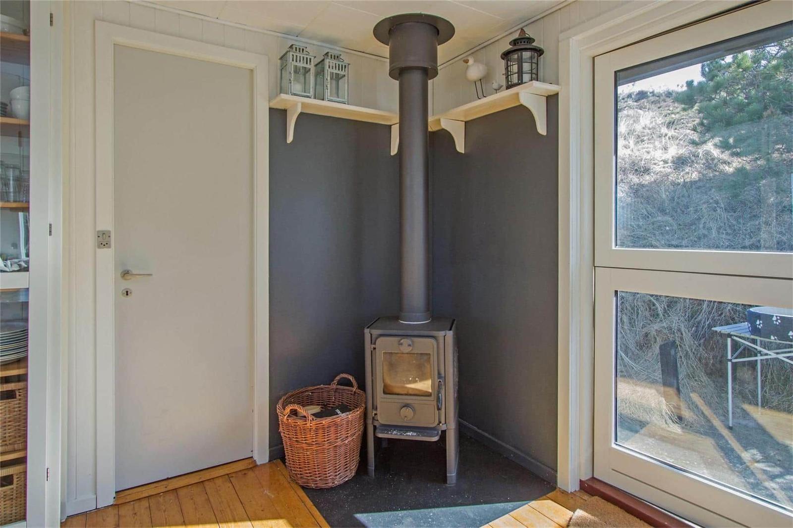 Room with wood stove, window, and door. Shelves on walls hold decorations.