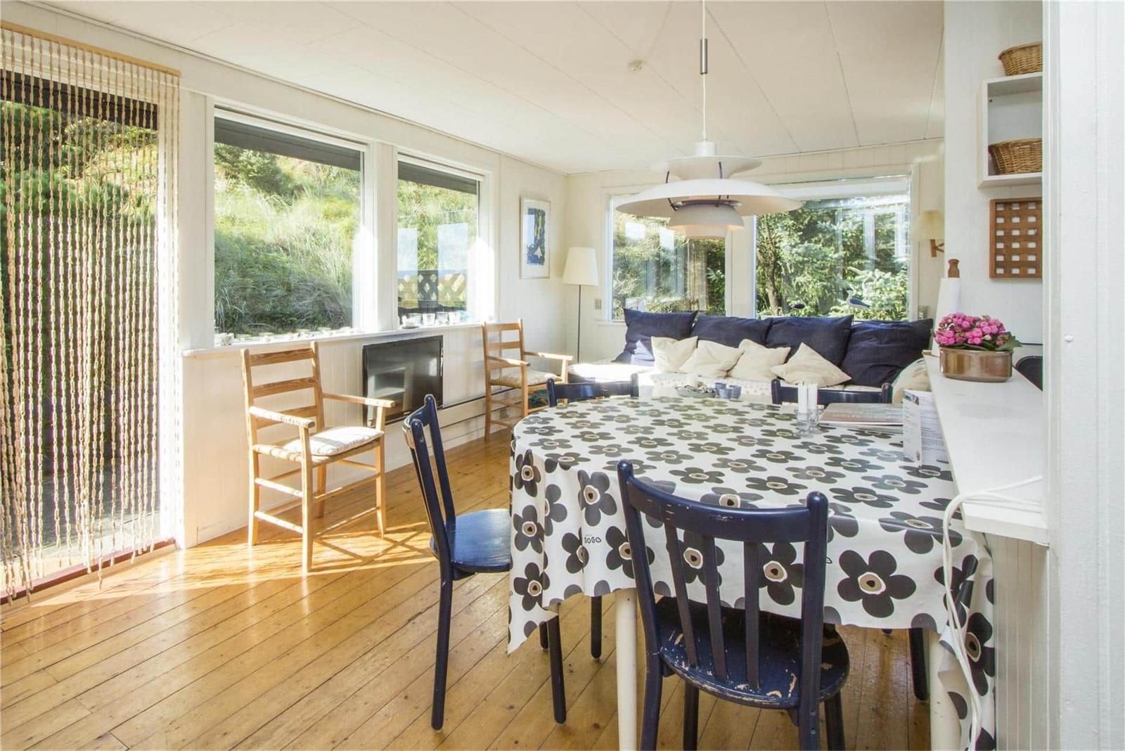 Dining area with table, chairs, and seating. Wooden floor and windows with view to greenery.