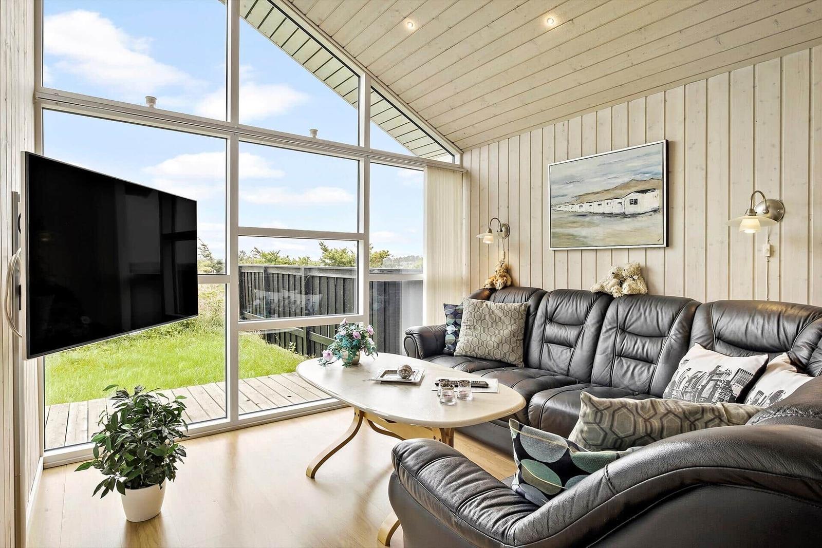 Wohnzimmer mit Ledersofa, TV und großem Fensterblick auf Grünfläche.