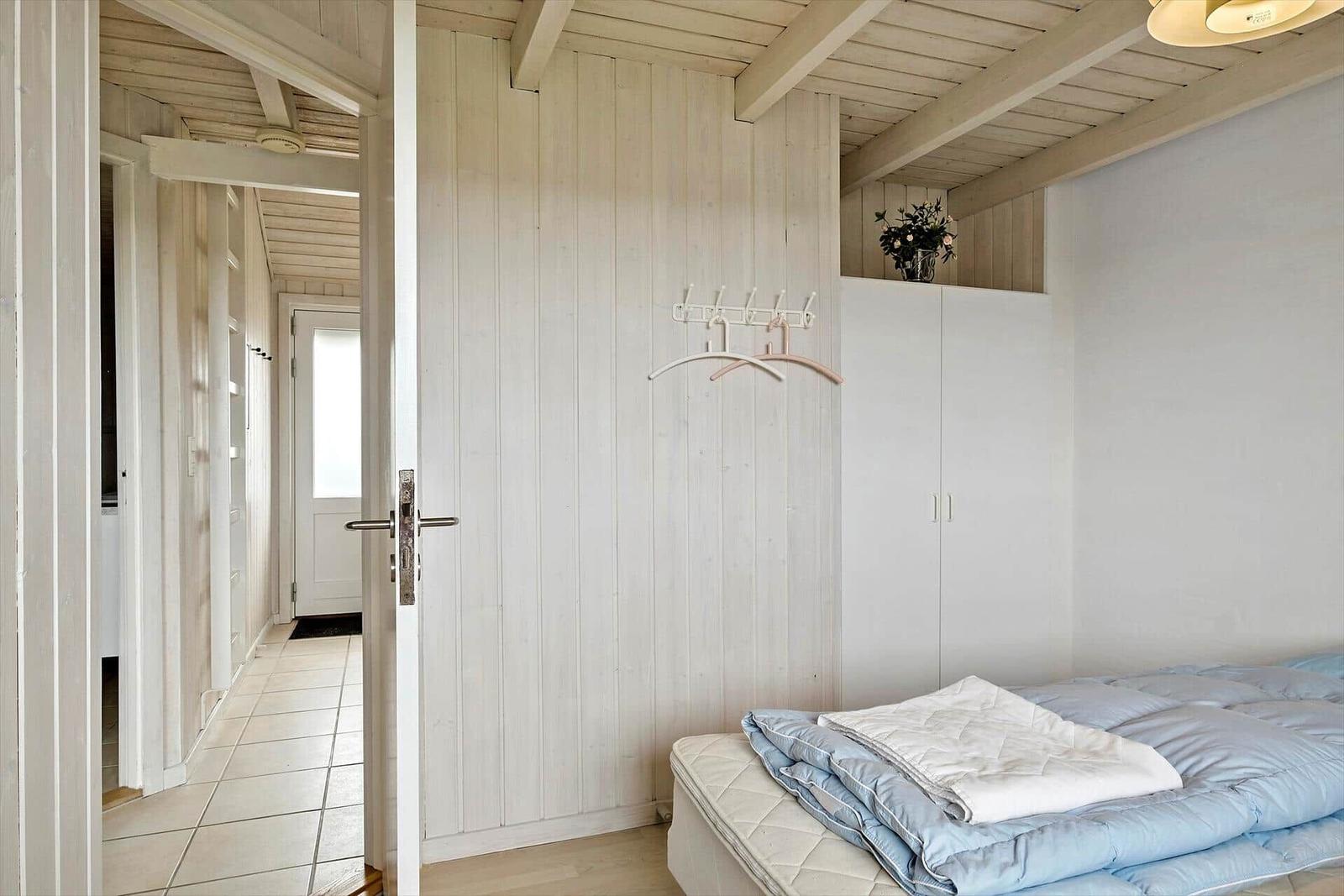 Schlafzimmer mit Bett, Kleiderhaken und Schrank. Durchgang zur Küche und Flur.