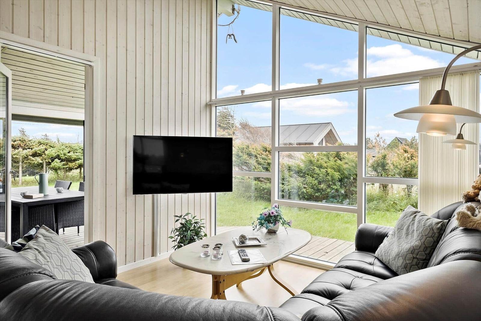 Wohnzimmer mit Sofa, TV und großem Fensterblick auf Garten.