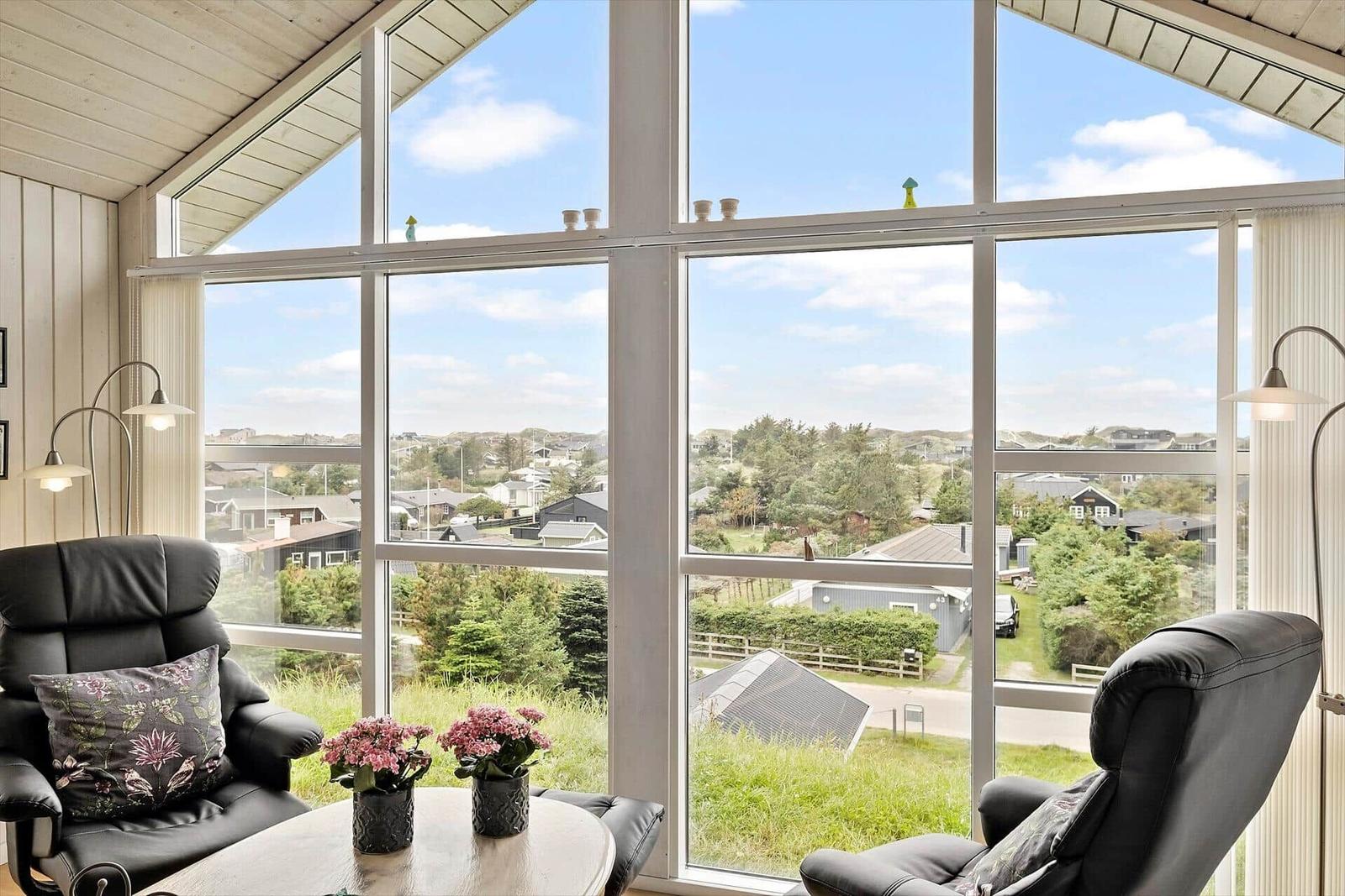 Zwei schwarze Sessel und ein Tisch vor großen Fenstern mit Blick auf Grünflächen und Häuser.