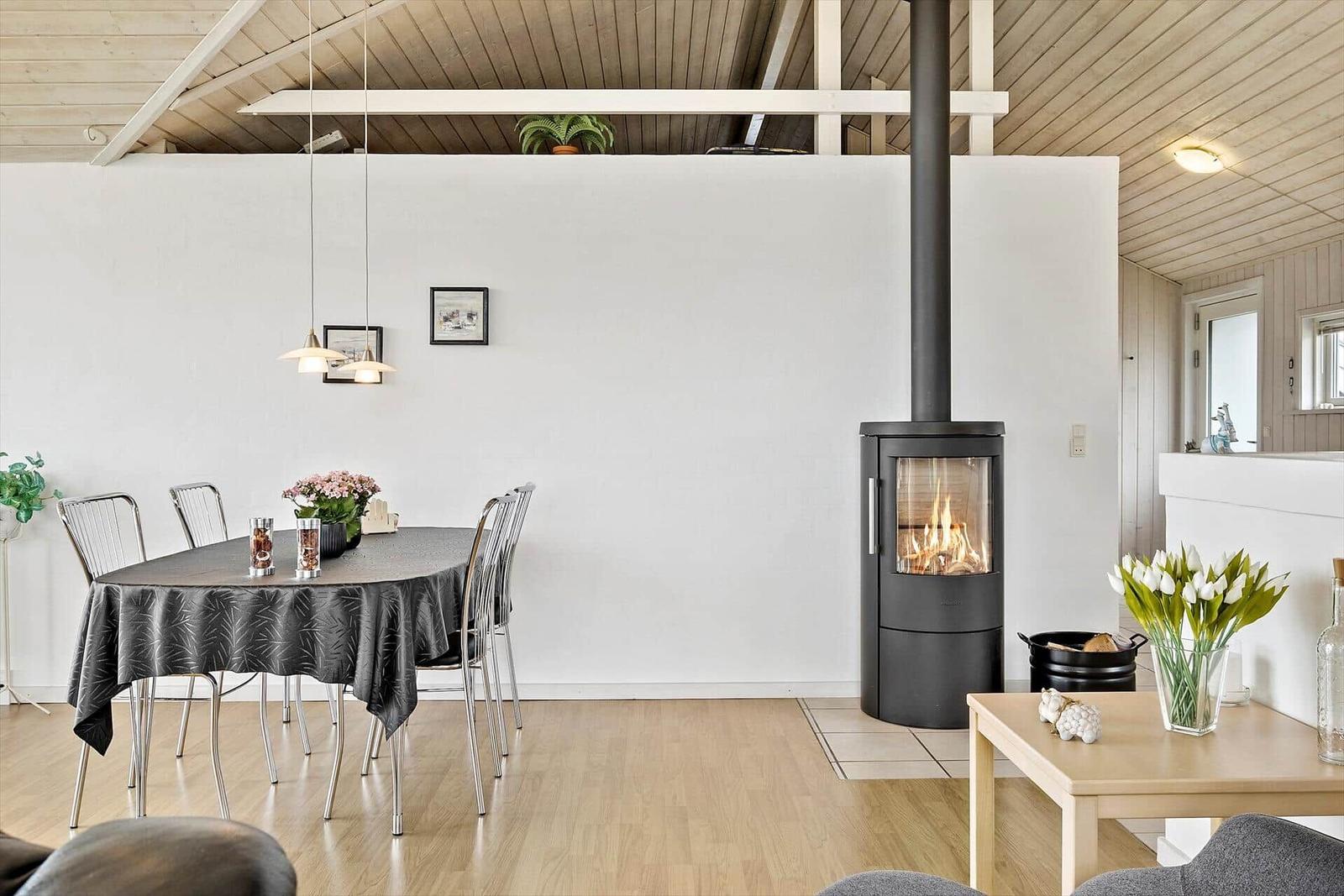 Essbereich mit Tisch, Stühlen und Kaminofen. Holzdecke und helle Wände.