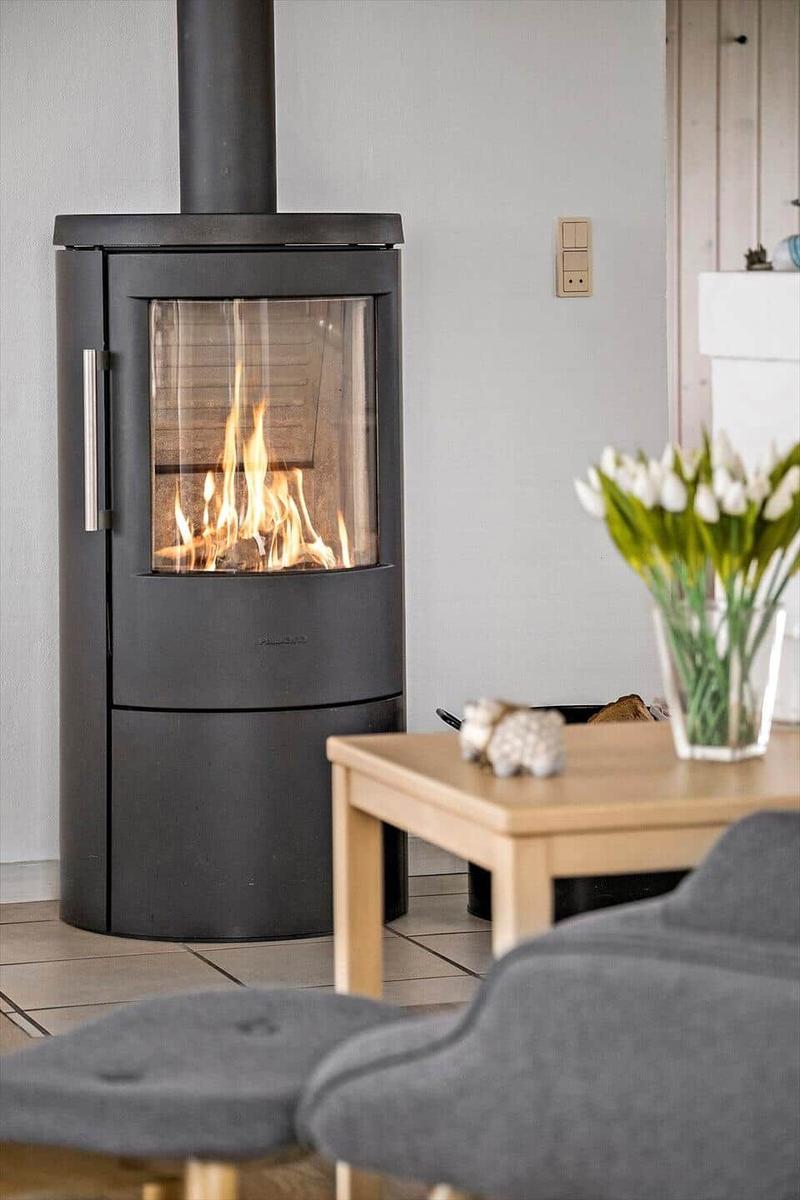 Kaminofen mit brennendem Feuer im Wohnbereich mit Tisch und Stühlen.