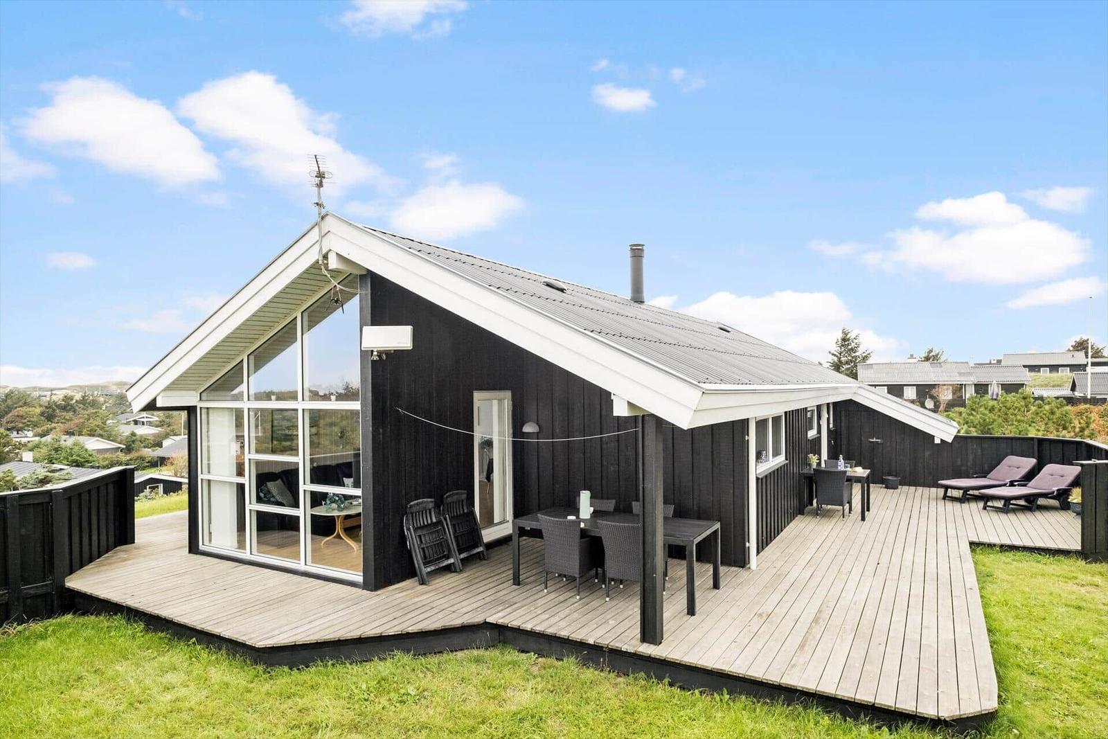 Moderne Holzhütte mit großem Balkon und Terrasse mit Sitzgelegenheiten.