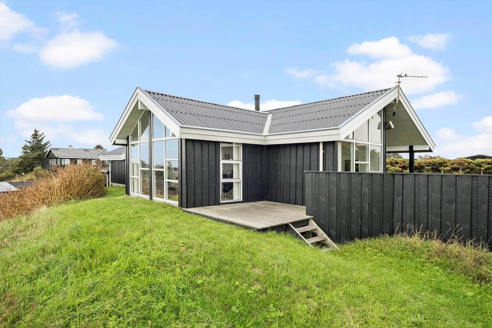 Moderne Villa mit Holzverkleidung und großem Fensterbereich auf grünem Grundstück.