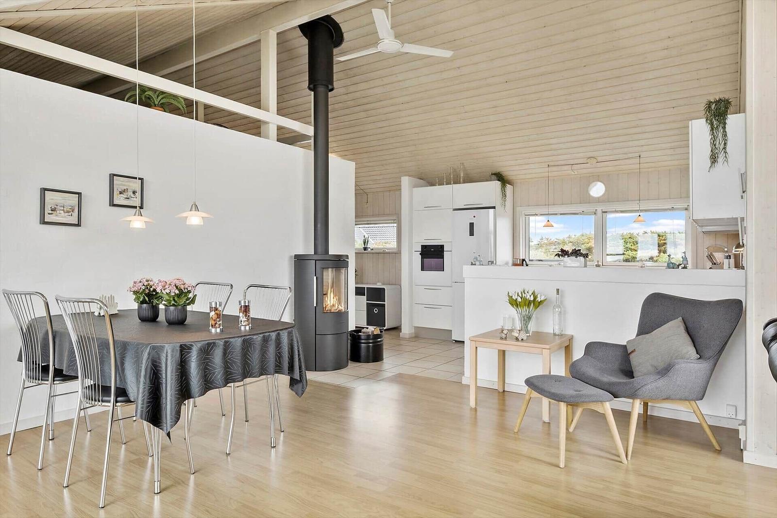 Wohnbereich mit Esstisch, Kamin und Küche. Holzboden und weiße Wände.