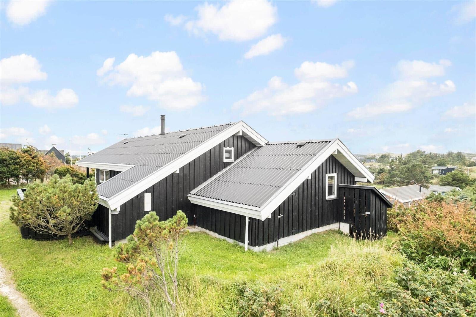 Schwarzes Holzhaus mit grauem Dach und weißem Putz, umgeben von Gras und Bäumen.