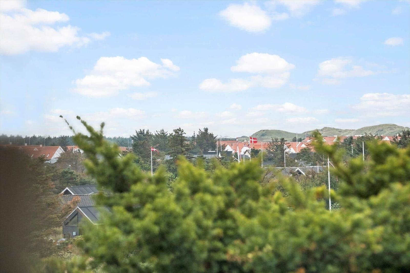 Panoramablick auf eine Siedlung mit roten Dächern und grünen Hügeln unter blauem Himmel.