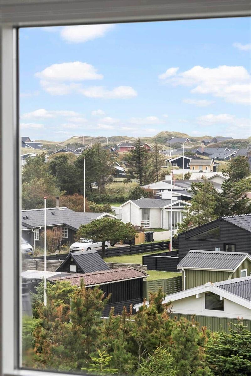 Aus dem Fenster sieht man Häuser und Grünflächen unter blauem Himmel mit weißen Wolken.