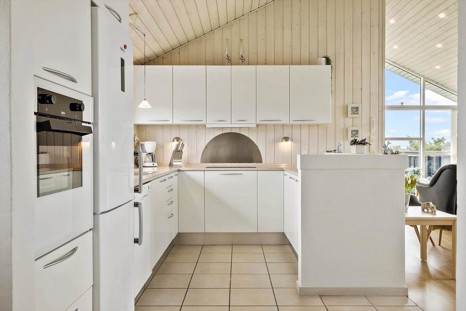 Küche mit weißen Schränken, Steinplatte und integriertem Ofen. Blick auf Wohnbereich.