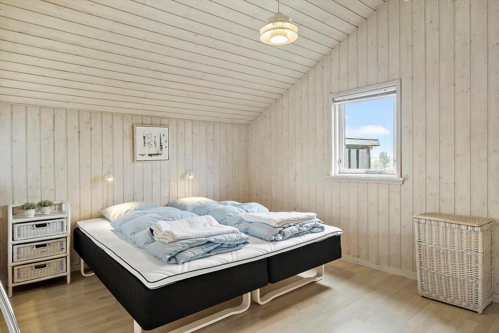 Schlafzimmer mit Bett, Nachttisch und Fenster.