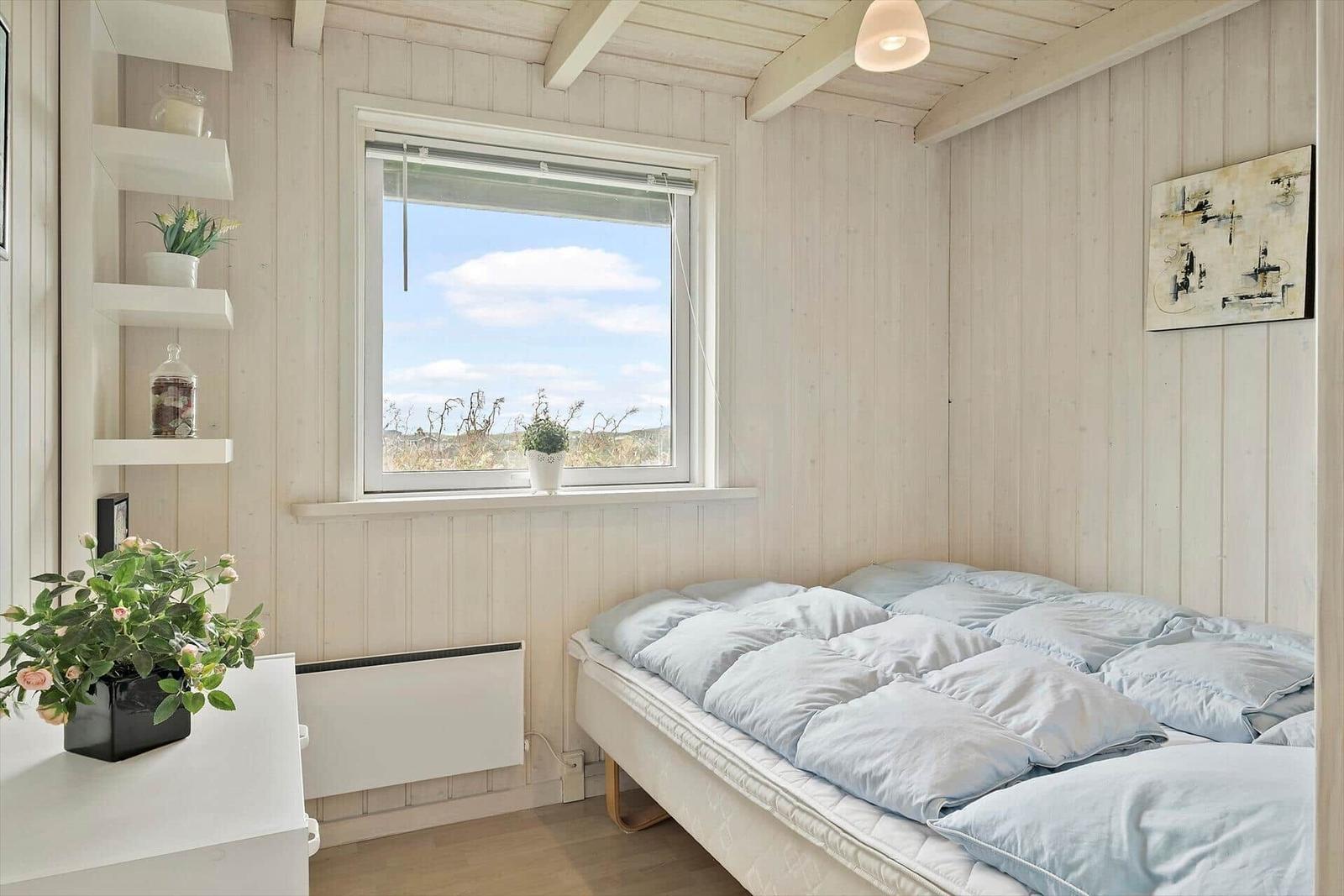 Schlafzimmer mit Bett, Fenster und weißen Wänden.