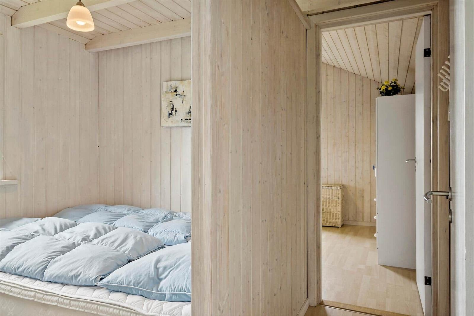 Schlafzimmer mit Bett und Holzwand. Durchgang zu einem Raum mit Schrank und Korb.