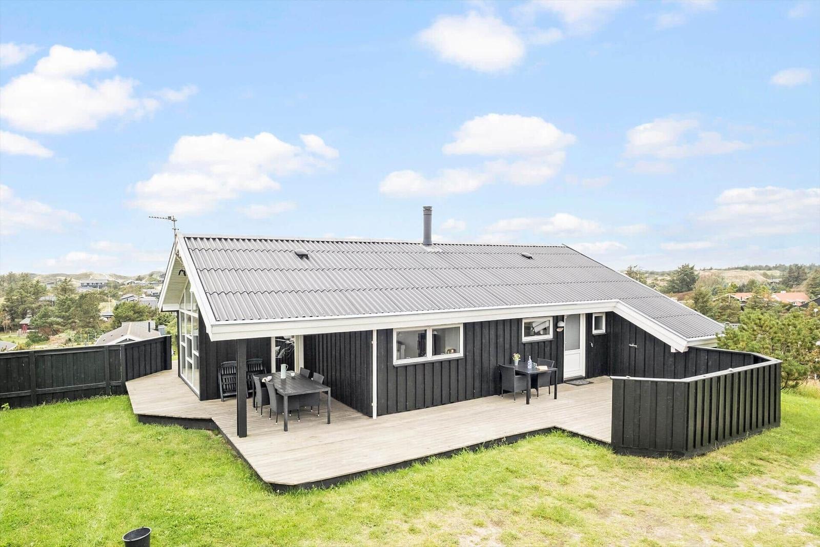 Ein Haus mit Holzterrasse und Garten. Außentisch und -stühle sind vorhanden.
