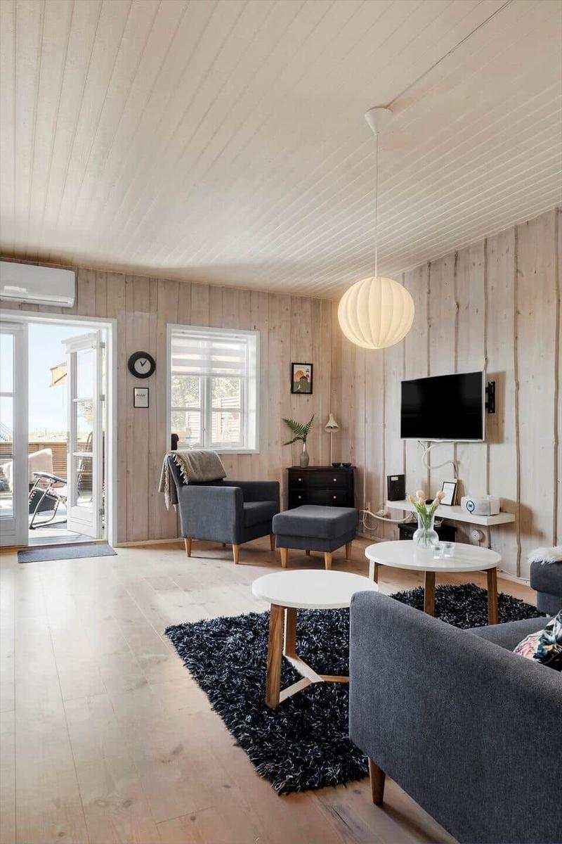 Living room with wooden walls, seating furniture, and TV mounted on the wall.