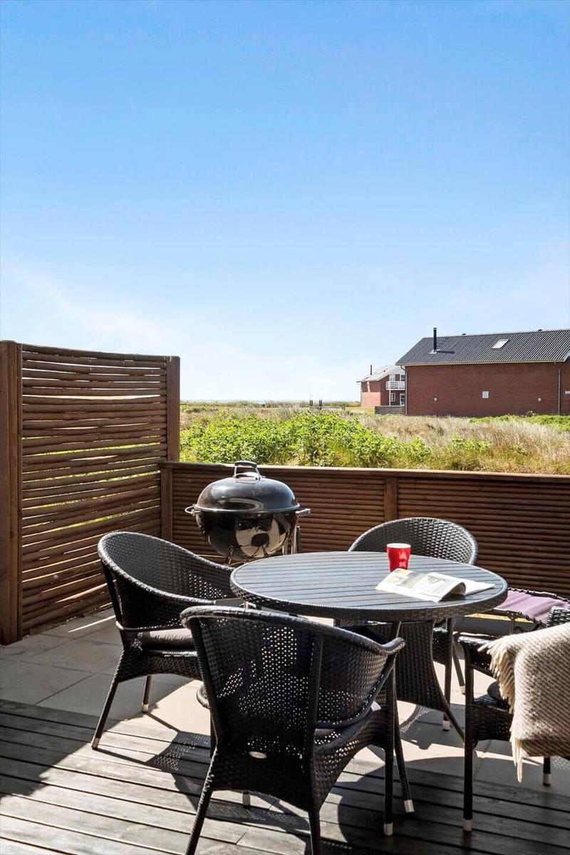 Deck with table, chairs, and grill. View of greenery and buildings.