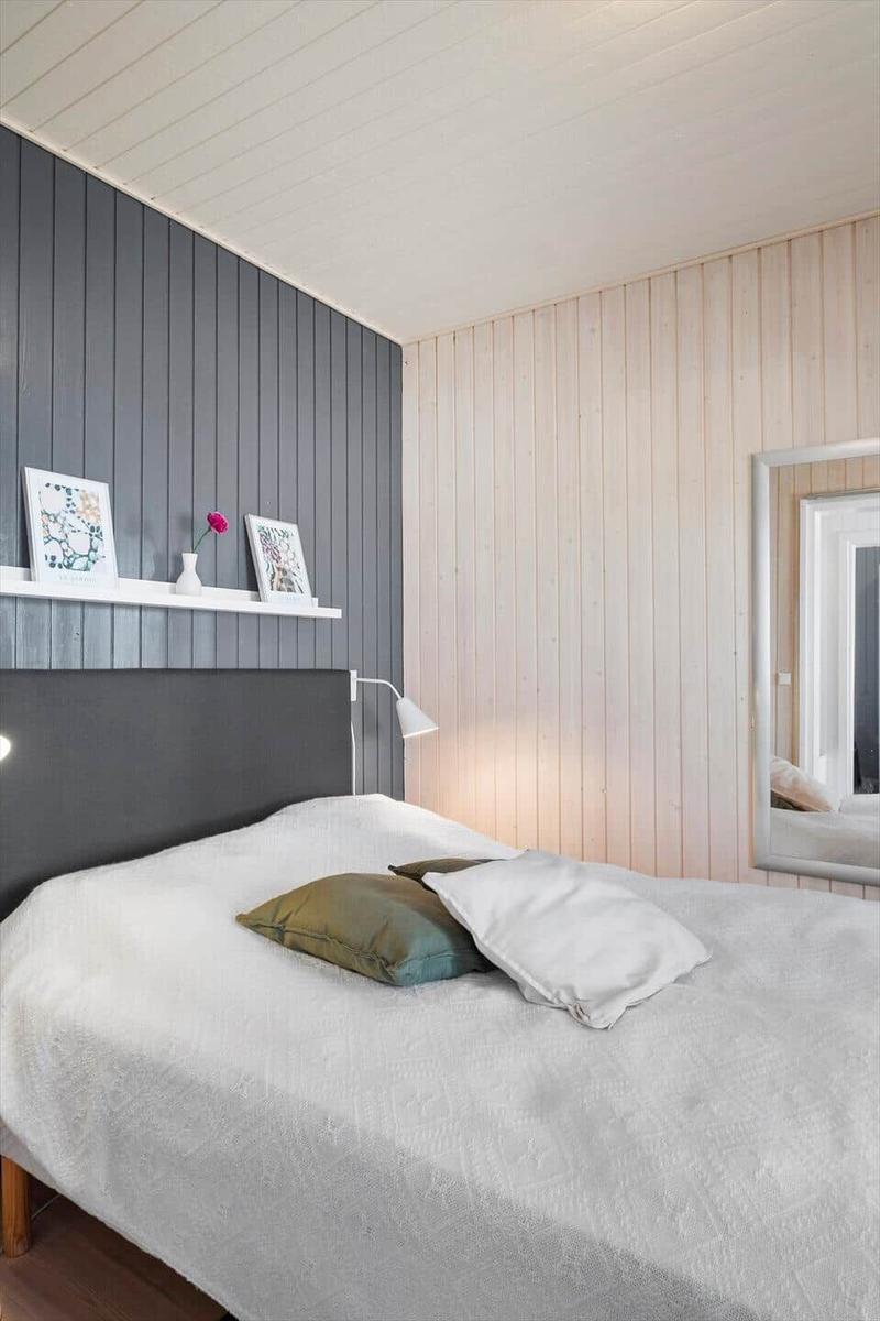Bedroom with bed, shelf, and mirror. Wooden wall and gray wall cladding.