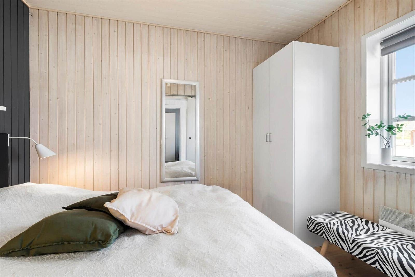 Bedroom with bed, wardrobe, and window. Wooden wall and zebra-patterned bench.