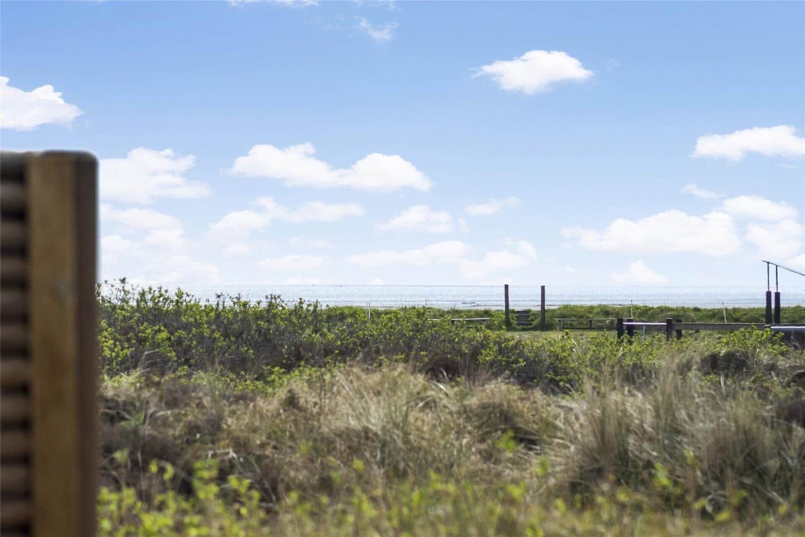 View of the sea through grass and a wooden fence.