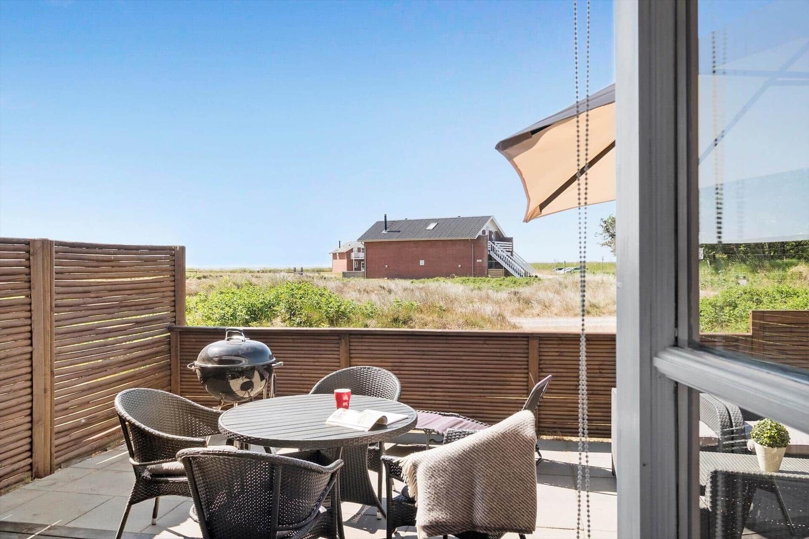 Terrace with table, chairs, and grill. View of a red barn and green area.