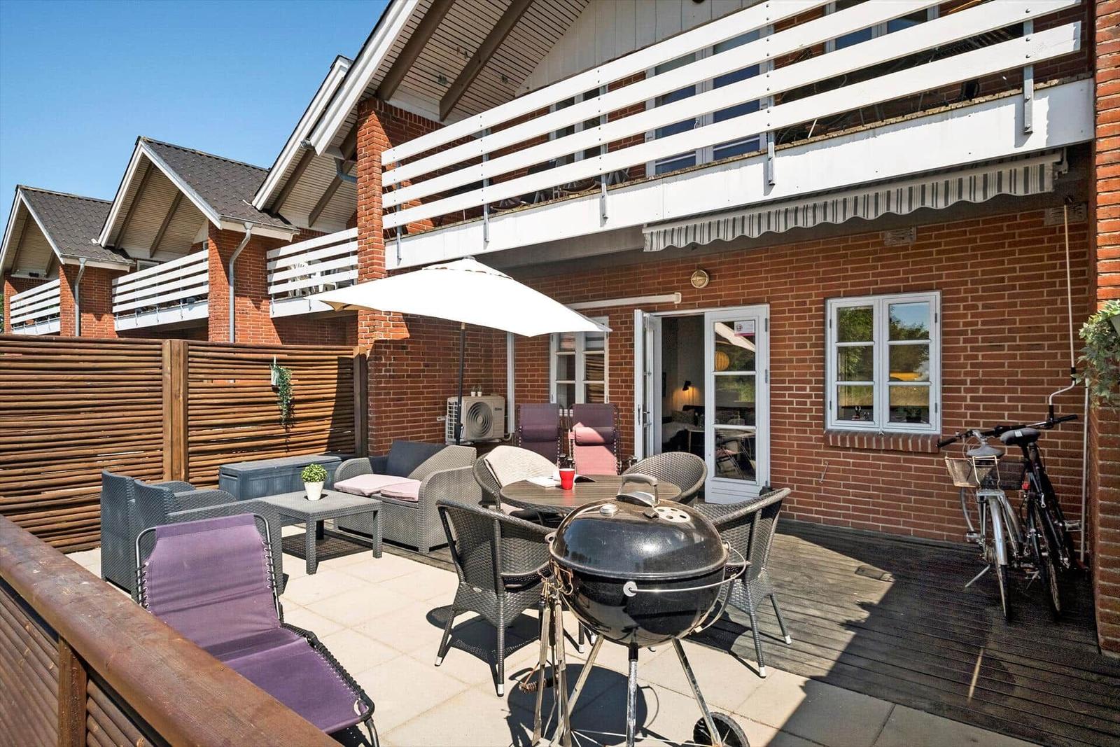 Terrace with grill, seating group, and table under umbrella. Bicycle and window are visible.