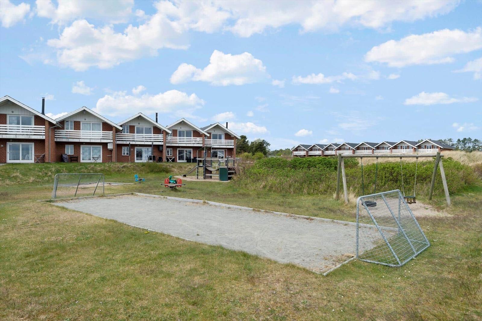 Green outdoor area with sandbox, swing, and soccer goal in front of holiday homes.