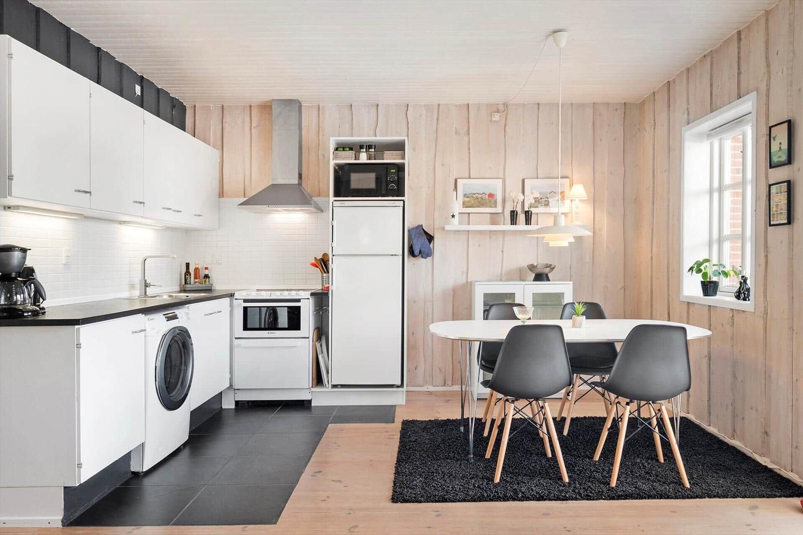 Kitchen with dining area, white cabinets, black countertop, and wooden wall.
