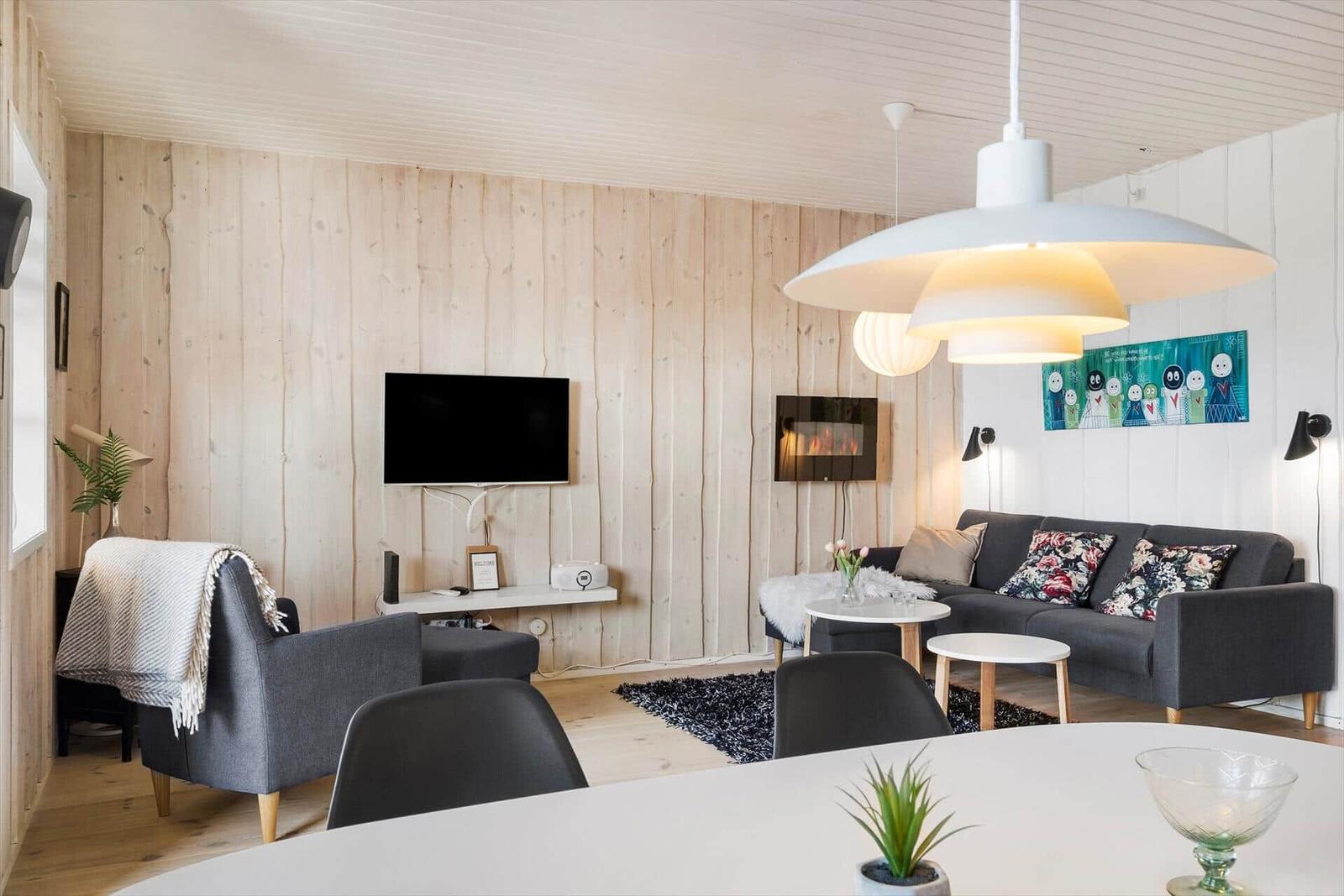 Living room with sofa, TV, and dining table. Wooden wall and ceiling.