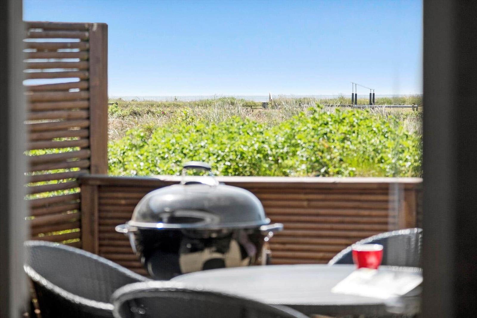 Terrace with grill, table, and chairs. View of green areas and horizon.