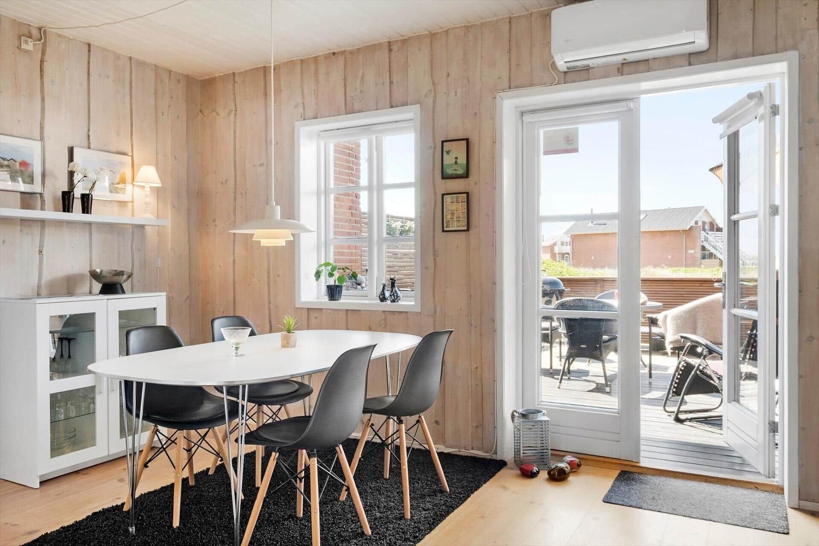 Dining room with white table, black chairs, and wooden walls. Glass door leads to the terrace.