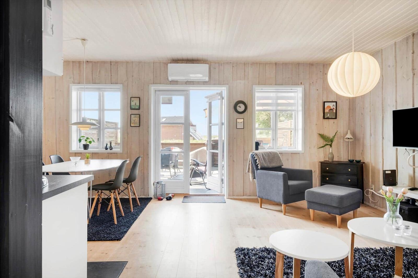 Living and dining area with wooden walls, windows, and door to outdoor area.
