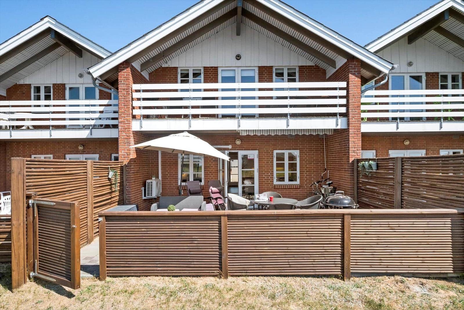 House with terrace, garden, and grill area. White balconies and red brick walls.