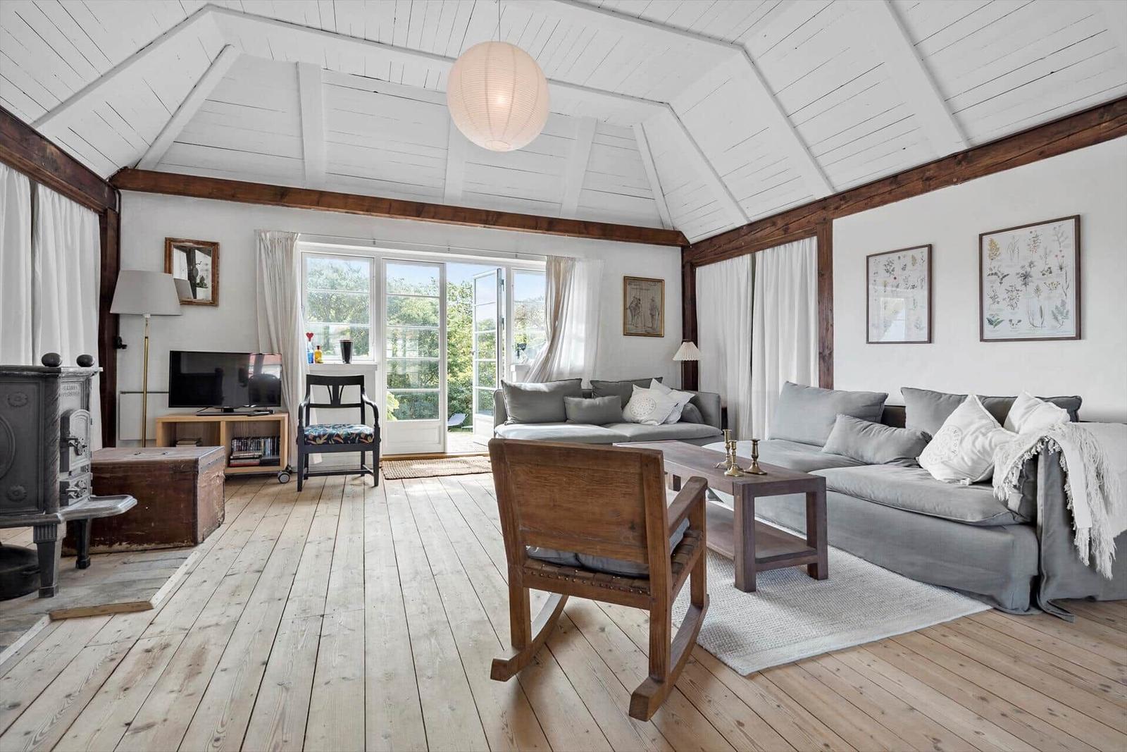 Wohnzimmer mit Holzboden, grauem Sofa und Schiebetür zum Garten.