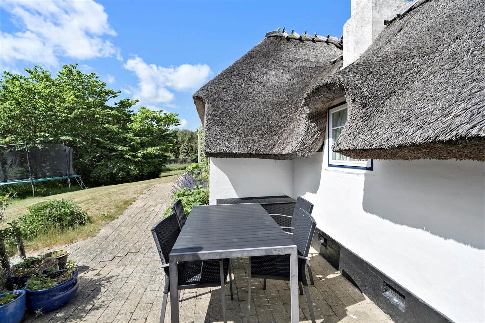 Terrasse mit Tisch und Stühlen neben einem Haus mit Strohdach.