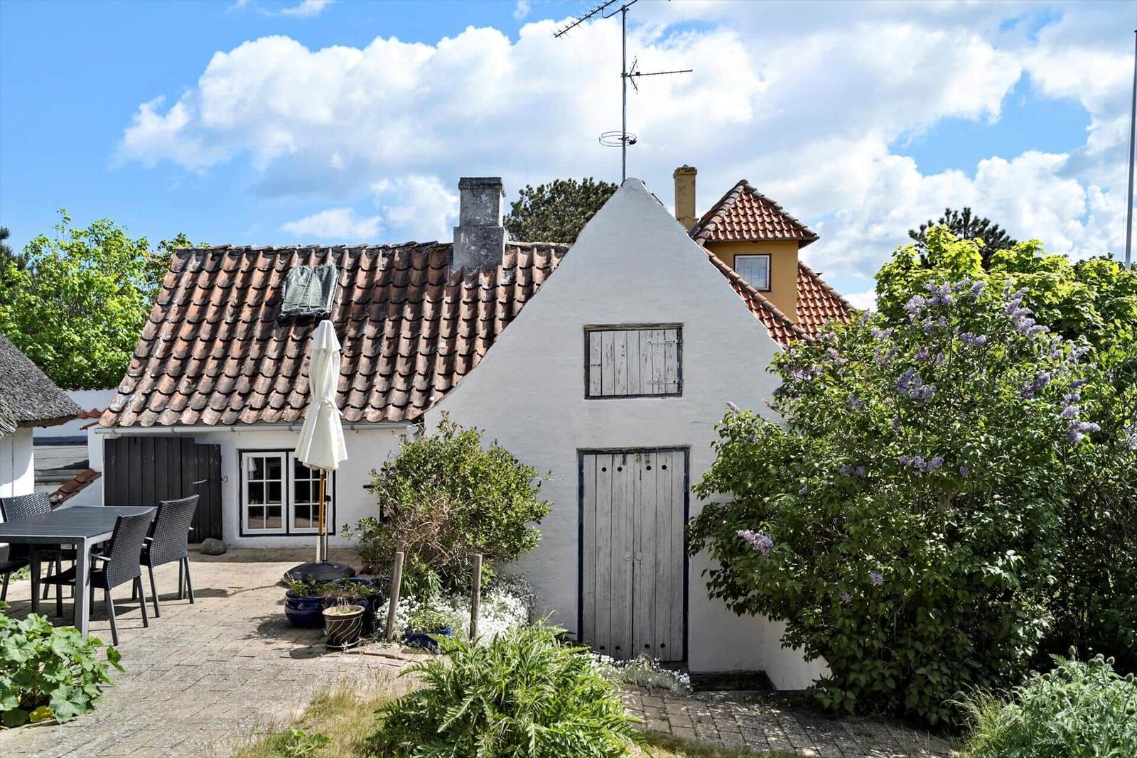 Wohnhaus mit Terrasse, Garten und Terrakottadach unter blauem Himmel.