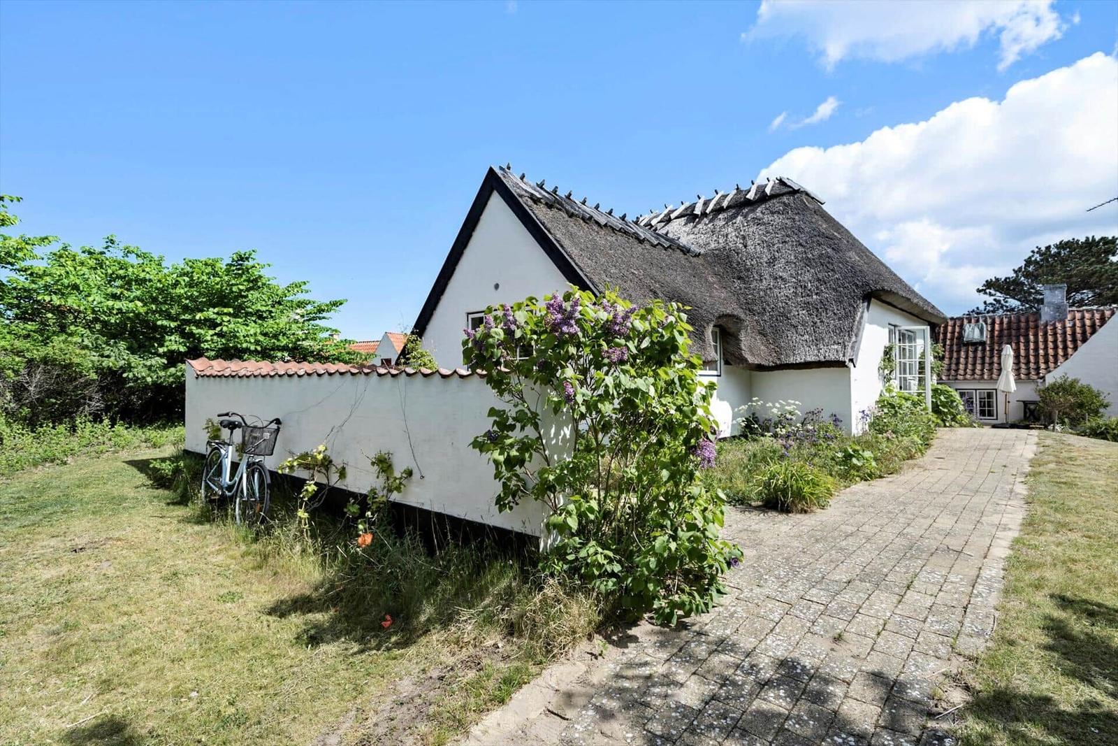 Wohnhaus mit Strohdach, gepflasterter Weg und Blumenbeet. Fahrrad an der Wand.