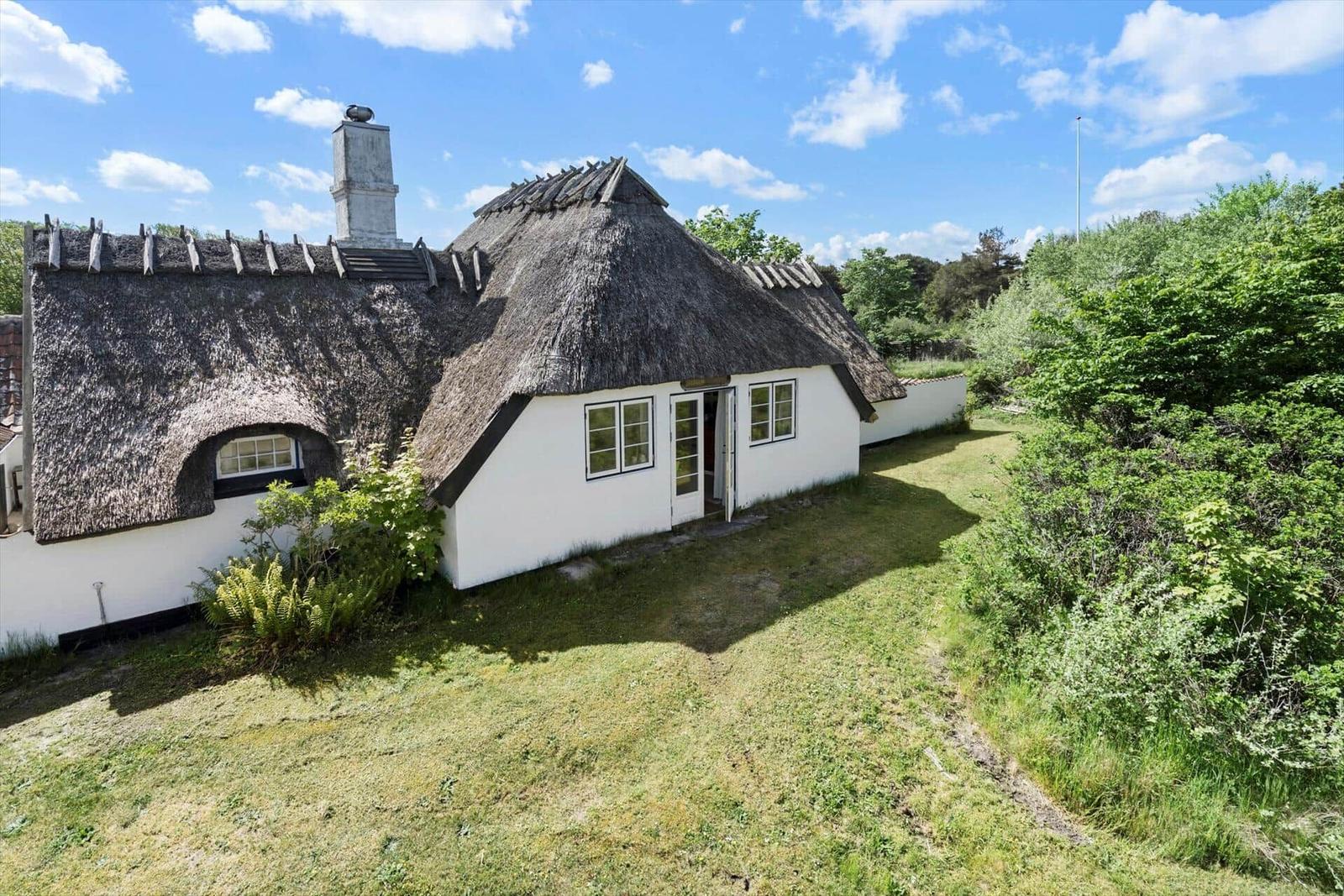Dorfhaus mit Strohdach, weißer Fassade und Garten.
