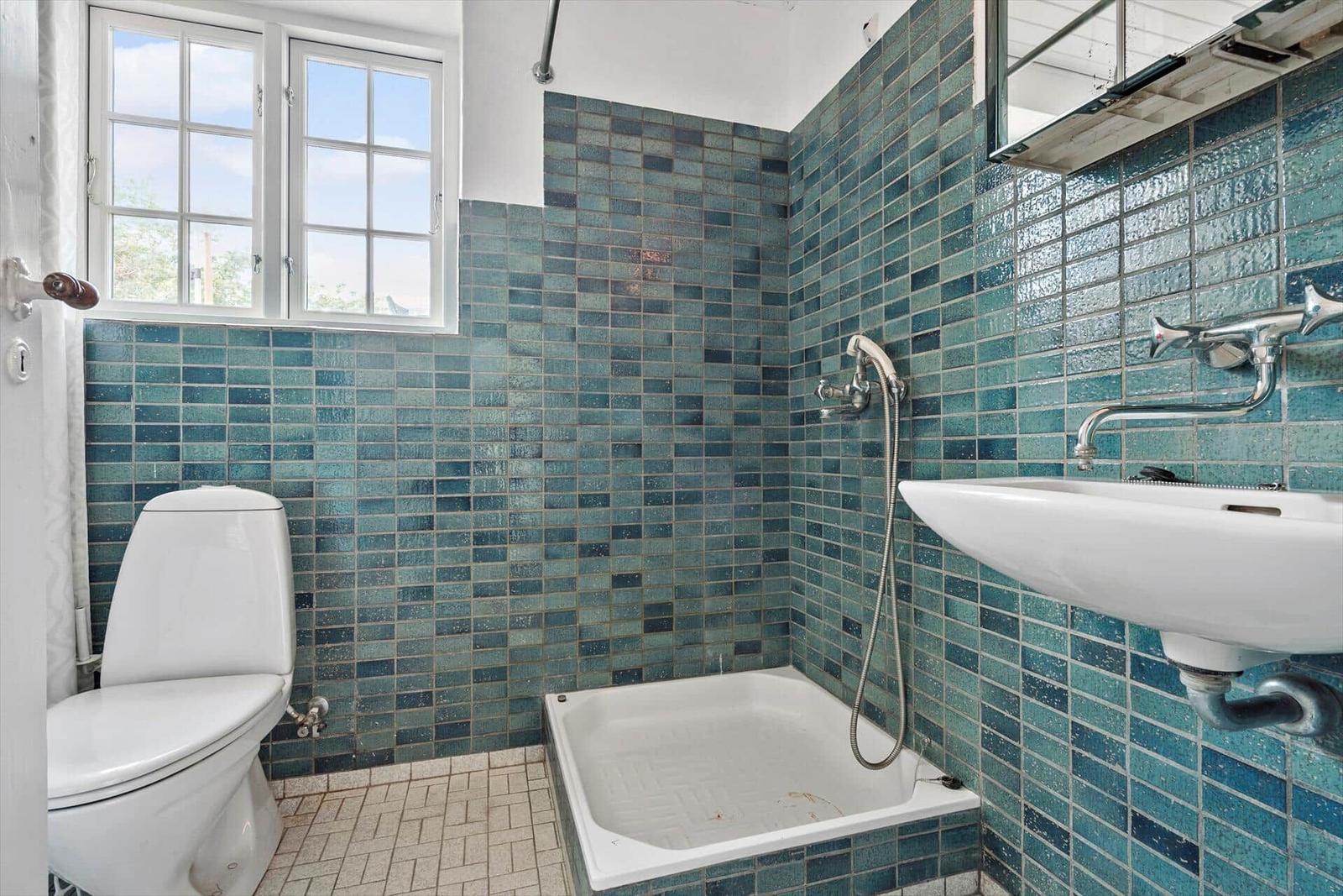 Badezimmer mit Badewanne, Toilette und Waschbecken. Wände mit blauen Fliesen.