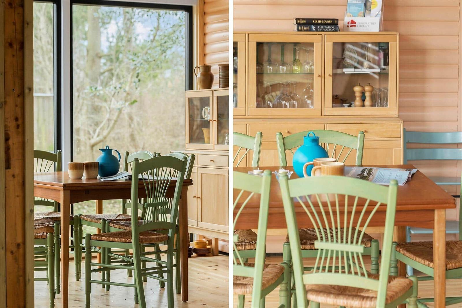Esszimmer mit Holztisch, grünen Stühlen und Glasvitrine. Große Fenster zeigen Wald.