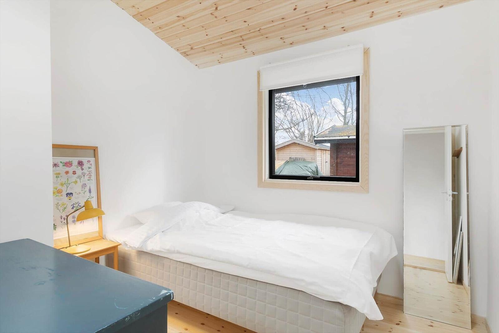 Ein Schlafzimmer mit Bett, Fenster und Spiegel. Holzdecke und Boden.