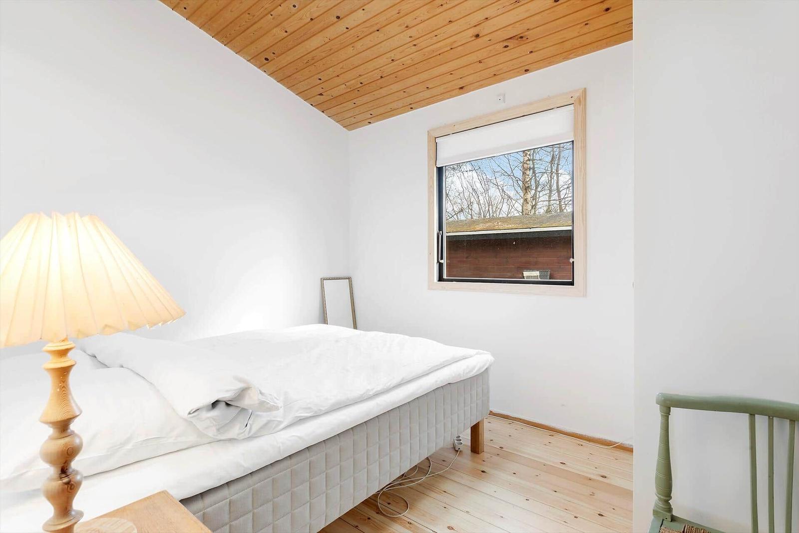Schlafzimmer mit Bett, Lampe und Fenster. Holzdecke und Boden.