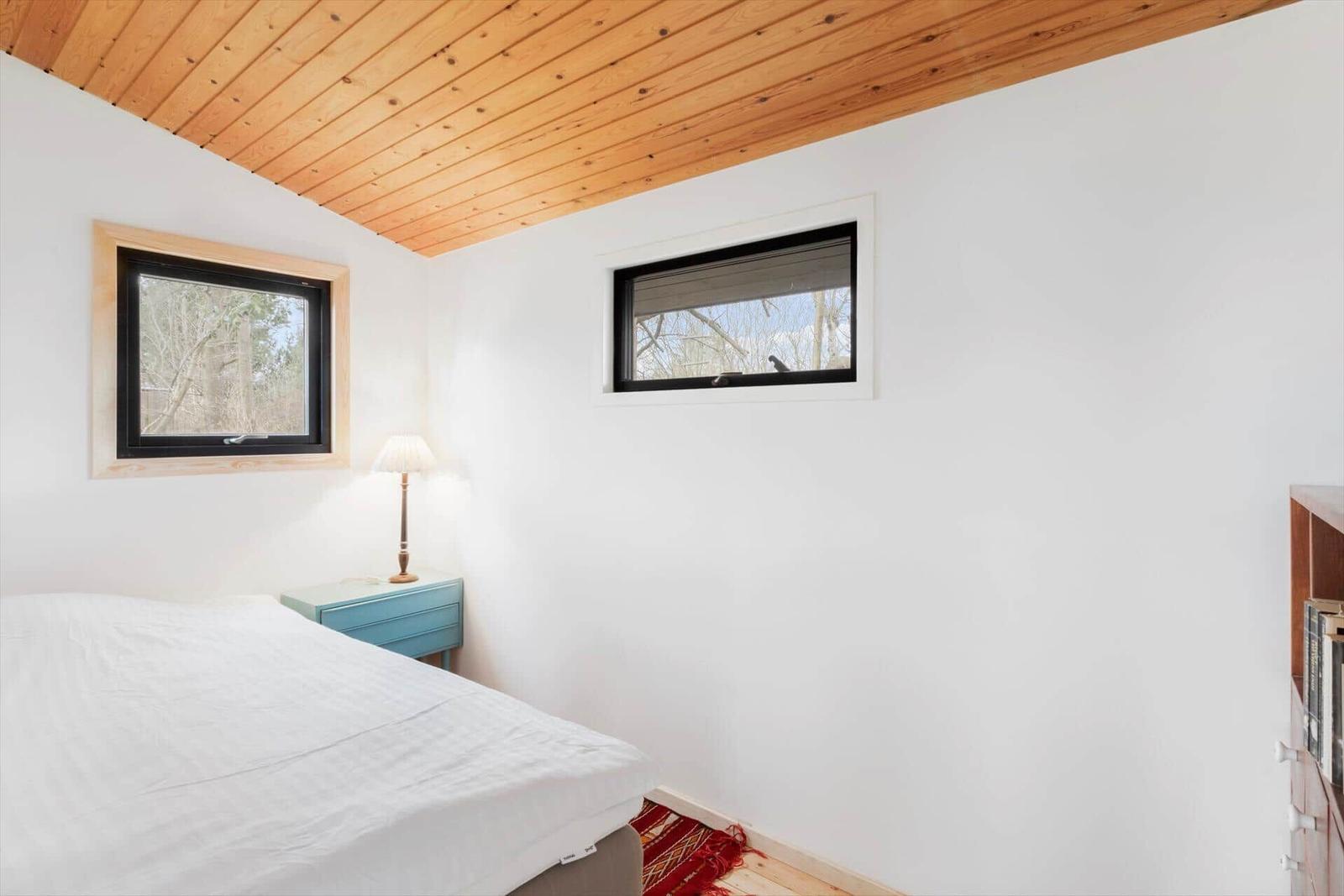 Schlafzimmer mit Holzdecke, zwei Fenstern und einem Bett mit weißer Bettwäsche.