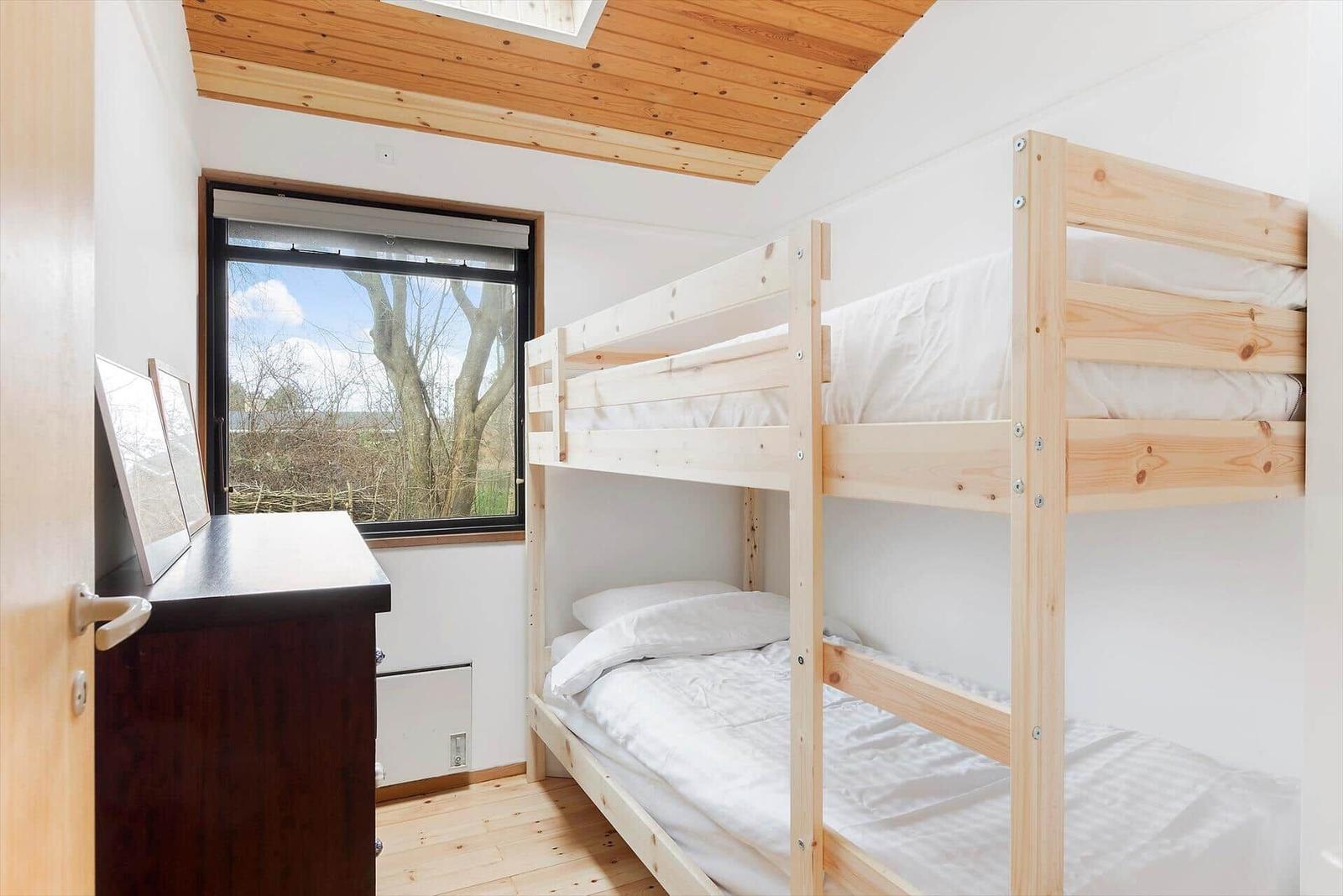 Zimmer mit Doppelstockbett, Fenster und Holzdecke.